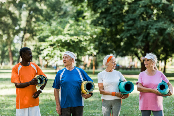 heureux retraités âgés et multiculturels tenant des tapis de fitness tout en se tenant dans le parc
  - Photo, image