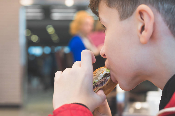 Jongen eten Fast Food in het café. Het concept van voedsel en ongezonde levensstijl. Frietjes in mand en grote hamburger met ketchup en saus - Foto, afbeelding