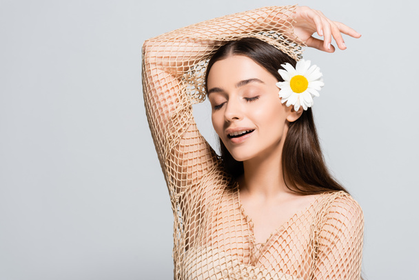 beautiful smiling woman with daisy in hair and closed eyes isolated on grey - Фото, изображение