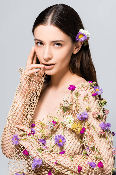 beautiful woman in mesh beige clothing with purple flowers touching lips isolated on grey - Foto, immagini