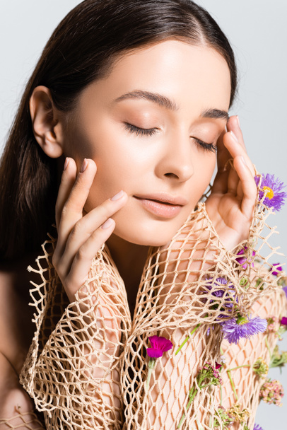 beautiful girl  with closed eyes in mesh beige clothing with purple flowers touching face isolated on grey - Foto, Imagen