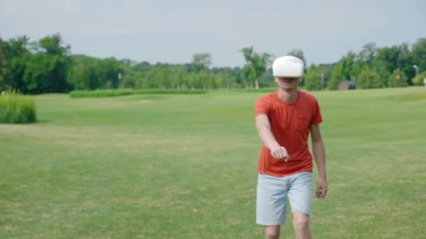Een man die een vr-headset gebruikt en een virtueel spel in het Park speelt. Jonge kerel in helm ervaren Augmented Reality op de achtergrond van de natuur. Een mens aan de rechterkant in het frame. 4k-beeldmateriaal. - Video