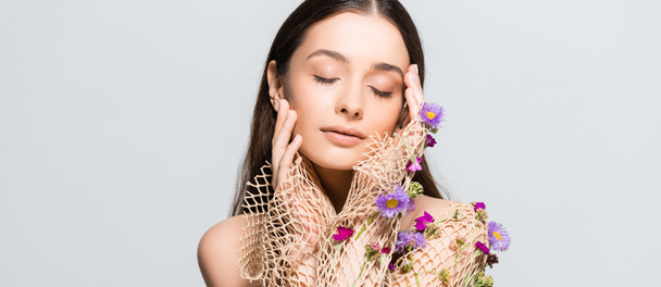 beautiful woman with closed eyes in mesh beige clothing with purple flowers touching face isolated on grey - Foto, afbeelding