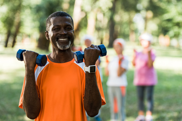 selective focus of happy african american man standing with dumbbells near pensioners  - Photo, Image