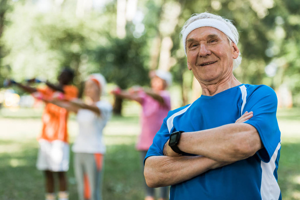 selective focus of happy senior man standing with crossed arms in park  - Photo, Image