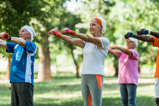 selective focus of senior pensioners exercising with dumbbells in park  - Fotografie, Obrázek