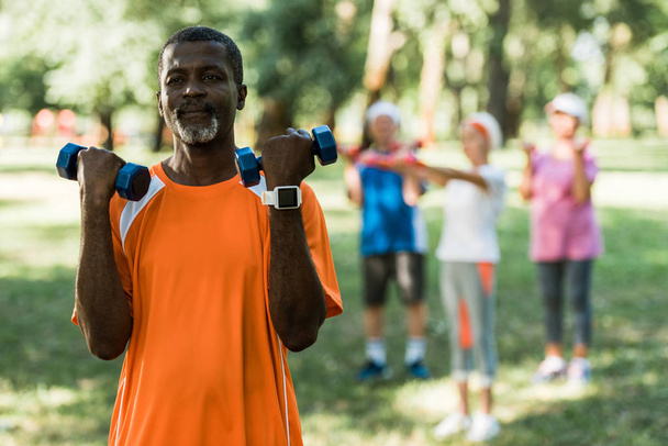 selective focus of senior african american man holding dumbbells while exercising in park  - Fotó, kép