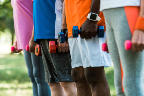 cropped view of multicultural pensioners in sportswear holding dumbbells in park  - Foto, imagen