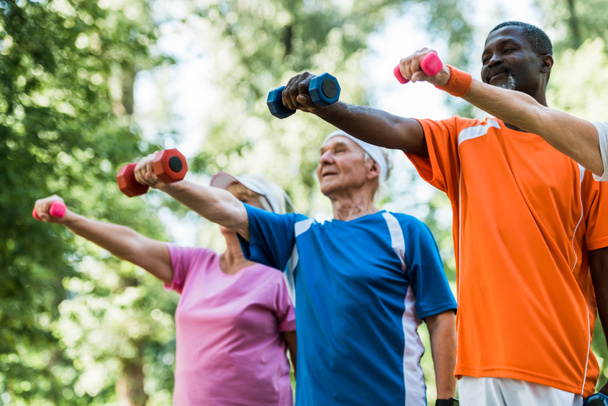 Низкий угол обзора пенсионеров в спортивной форме тренировки с гантелями в парке
  - Фото, изображение