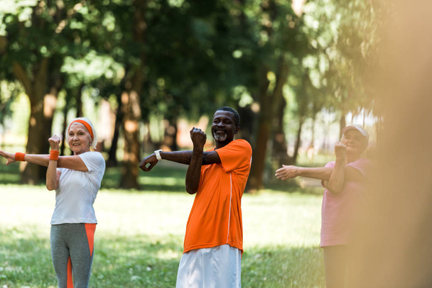 selective focus of happy milticultural retired women and man working out in park  - Foto, Imagen