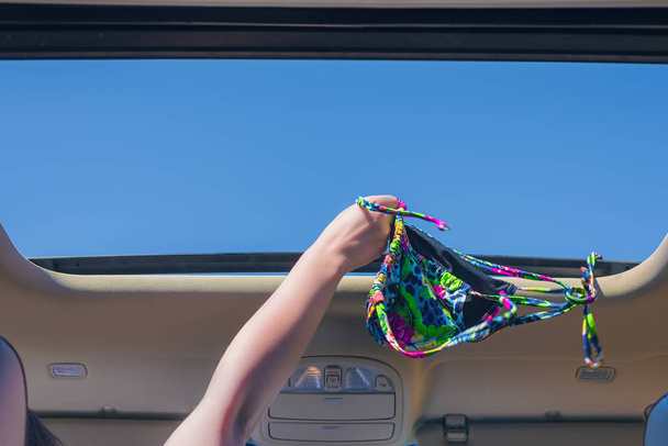 girl trowing away her bikini bra out from open hatch of a vehicle. Travel lifestyle concept - Photo, Image