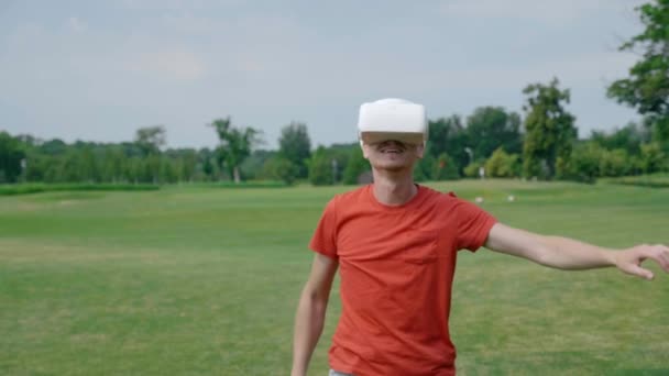 Człowiek za pomocą gogli VR i grając wirtualną grę w parku. Młody facet w hełmie doświadcza rozszerzonej rzeczywistości na tle natury. Człowiek po prawej stronie w ramce. materiał filmowy 4K. - Materiał filmowy, wideo