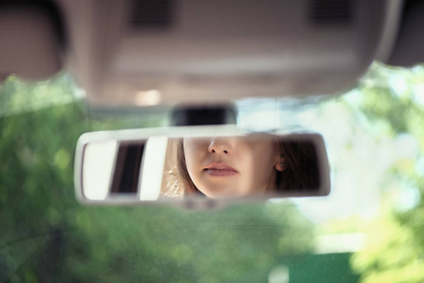 Αντανάκλαση ενός χαμογελαστή χειλιών νεαρής γυναίκας στον καθρέφτη της οπίσθιας προβολής του αυτοκινήτου. Έννοια. - Φωτογραφία, εικόνα