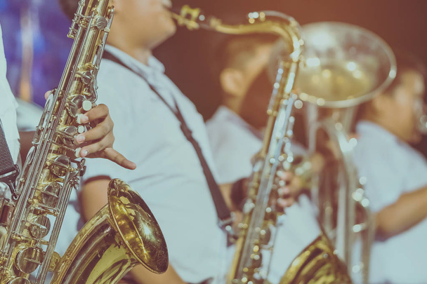 Mannelijke student met vrienden blazen de saxofoon met de band voor prestaties op het podium 's nachts. - Foto, afbeelding