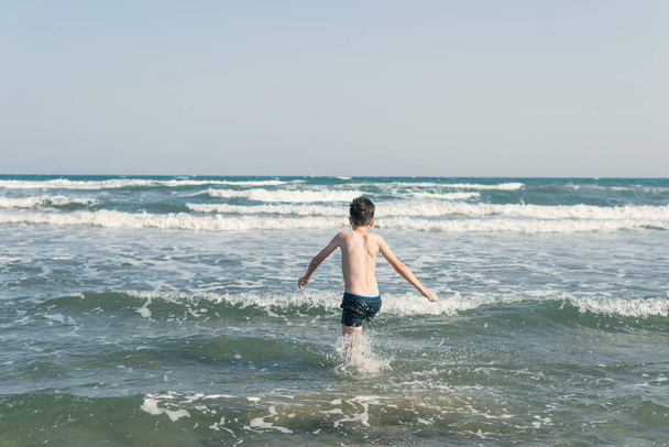 Мальчик на пляже в морских волнах с брызгами воды. Концепция летних каникул
 - Фото, изображение
