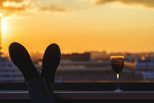 Silhouette of man feet with glass of red wine on the balcony on the city background - Fotó, kép
