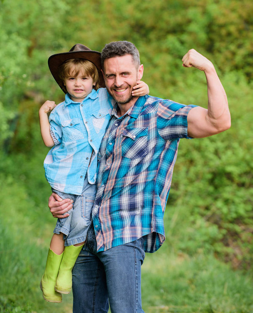 Child having fun cowboy dad. Rustic family. Growing cute cowboy. Small helper in garden. Little boy and father in nature background. Spirit of adventures. Strong like father. Power being father - 写真・画像