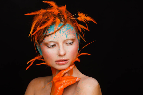 Portrait of a beautiful model with creative make-up and hairstyle using orange feathers - Fotó, kép