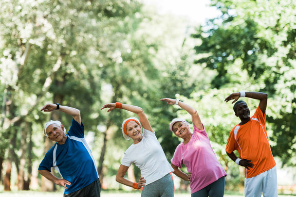 весёлые мультикультурные пенсионеры и женщины, стоящие с руками на бедрах во время упражнений на растяжку
  - Фото, изображение