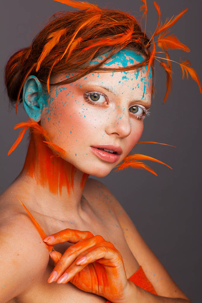 Portrait of a beautiful model with creative make-up and hairstyle using orange feathers - Photo, image
