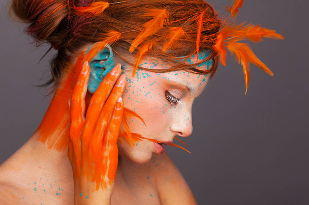 Portrait of a beautiful model with creative make-up and hairstyle using orange feathers - Foto, Imagem