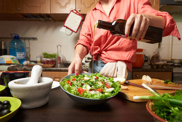 Женщина добавляет оливковое масло в здоровый греческий салат
 - Фото, изображение