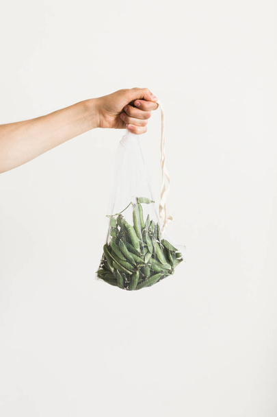 Reusable eco-friendly bag full of fresh seasonal pea pods on white background - 写真・画像