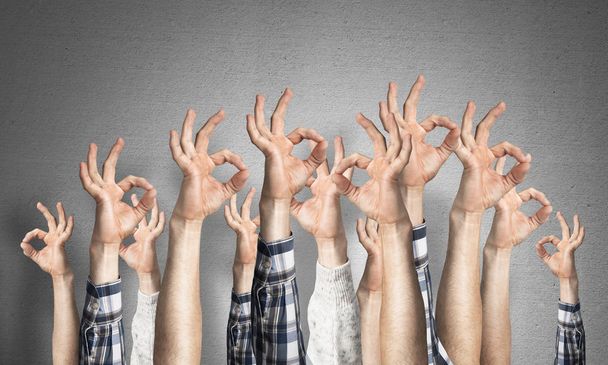 Row of man hands showing okay gesture. Agreement and approval group of signs. Human hands gesturing on background of grey wall. Many arms raised together and present popular gesture. - Photo, Image