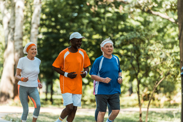 hombres mayores multiculturales felices y mujer jubilada corriendo en el parque
  - Foto, Imagen