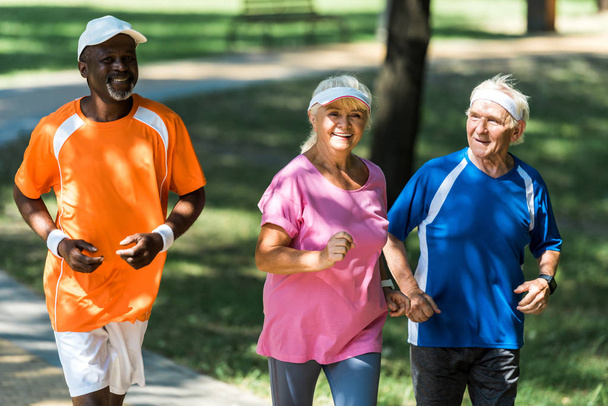 selective focus of happy retired woman running with multicultural men  - Photo, Image