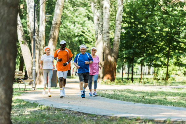 selective focus multicultural senior men and women in sportswear jogging in walkway in park  - Photo, Image