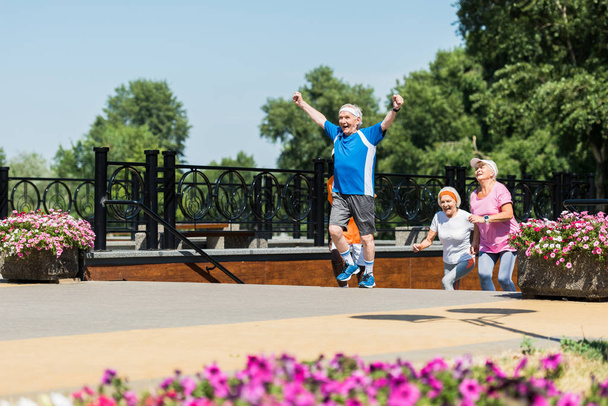 επιλεκτική εστίαση του ευτυχικού συνταξιούχου που γιορτάζει τον θρίαμβο κοντά σε πολυπολιτισμικούς συνταξιούχους στο πάρκο  - Φωτογραφία, εικόνα