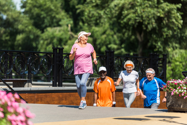 foco seletivo de mulher aposentada feliz correndo perto de pensionistas multiculturais seniores
  - Foto, Imagem