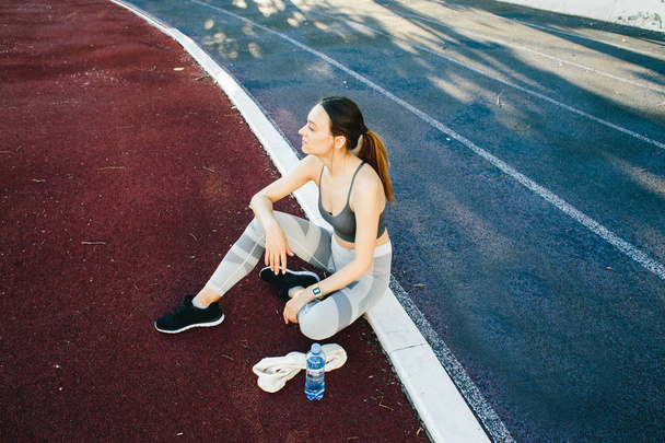 Jolie femme assise sur le sol avec une bouteille d'eau après avoir fait du jogging à l'extérieur
 - Photo, image