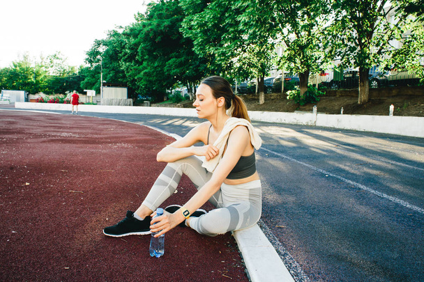 Bella donna seduta a terra con una bottiglia d'acqua dopo aver fatto jogging all'aperto
 - Foto, immagini