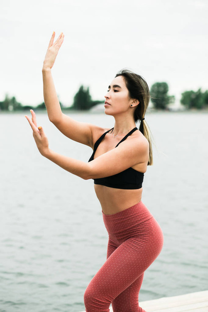 Asiática joven haciendo yoga al aire libre en el muelle por el lago
. - Foto, imagen