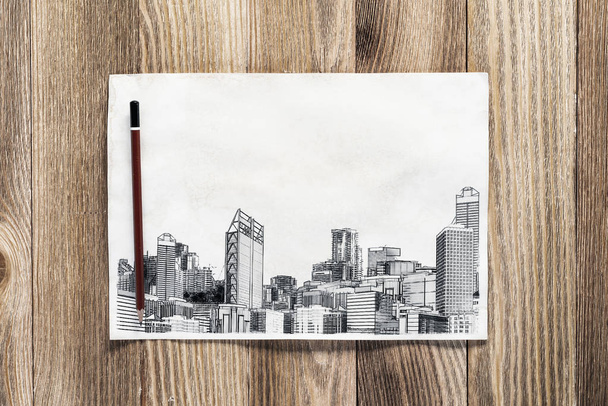 Σχεδίαση μολυβιού σε μεγάλη πόλη. Μοντέρνο τοπίο στο κέντρο της πόλης με ψηλούς ουρανοξύστες σκίτσο σε ξύλινη επιφάνεια. Χαρτί και μολύβι σε φυσικό ξύλινο φόντο. Έννοια μεσιτικού γραφείου. - Φωτογραφία, εικόνα