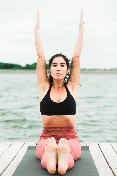 Asian young girl doing yoga outdoors on the pier by the lake. - Photo, Image