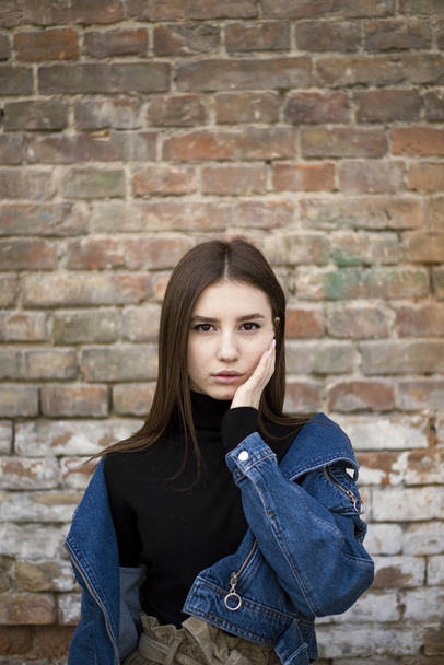 Portrait of a young caucasian girl with freckles. Jean jacket and skirt. Old Brick wall on background. Desaturated colors - Photo, Image