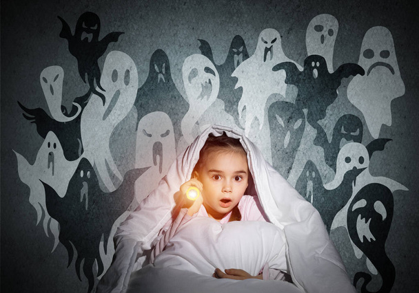 Surprised girl with flashlight hiding under blanket. Amazed kid sitting in his bed at home. Fear of the dark. Little child in pajamas afraid of ghosts at night. Nightmare fantasy and imagination. - Photo, image
