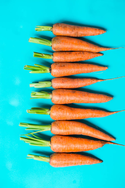varias zanahorias frescas se encuentran en una fila sobre un fondo azul
. - Foto, imagen