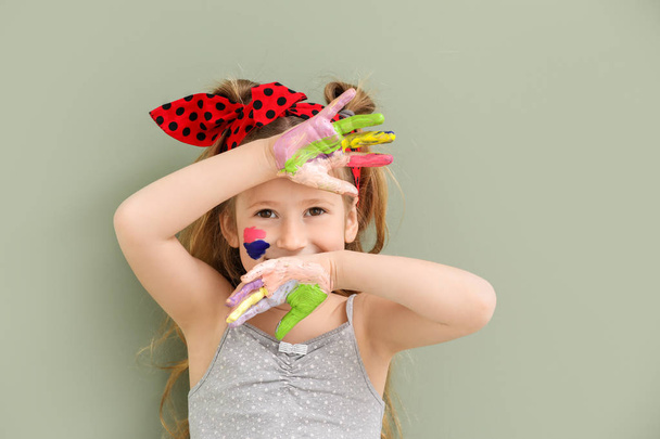 Cute little girl with hands and face in paint on color background - Foto, imagen
