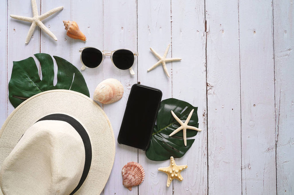 hat with sunglasses and smartphone with seashells on white wooden table background, top view - Photo, Image