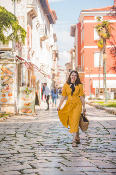 woman in yellow dress with bit straw hat walking by old tourist city in croatia - Photo, Image