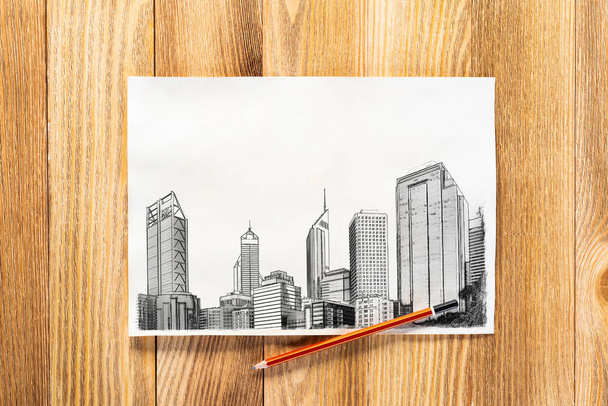 Modern city center pencil draw. Panorama of urban modern city with high skyscrapers sketch on wooden surface. Sheet of paper on textured natural wooden background. Architecture agency concept - Foto, afbeelding