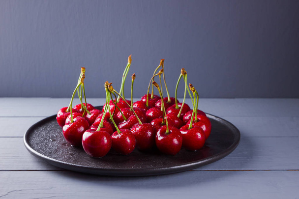 Cherries on a gray background. Red cherries on black plate. Berries in drops of water on wooden boards. Healthy food. Copy space - Foto, Imagem