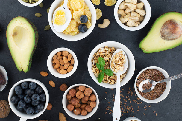 Ingredients for a healthy breakfast, nuts, oatmeal, flaxseed, dried fruit, avocado, egg, quinoa, cornflakes, berries, fruits, blueberry, almonds walnuts The concept of natural organic food in season - Φωτογραφία, εικόνα