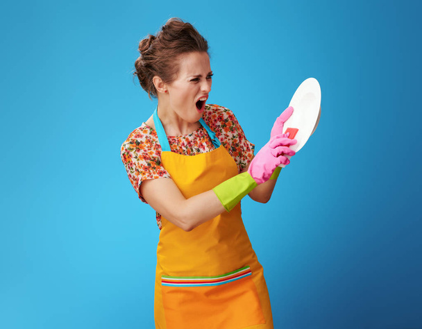 angry young woman with sponge washing dish on blue - 写真・画像