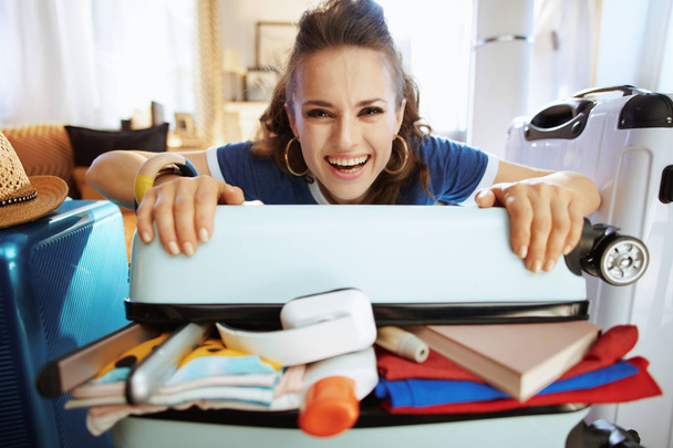 smiling traveller woman trying to close over packed suitcase - Foto, Imagem