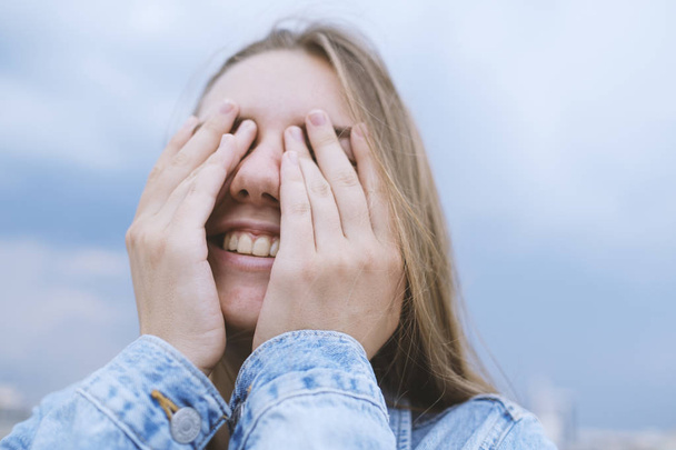 Молодая женщина закрывает глаза руками. Положительные эмоции, смех, улыбка, радость
 - Фото, изображение
